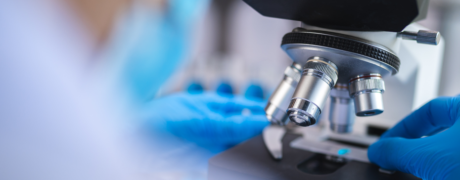 Gros plan sur un microscope au laboratoire, avec des mains portant des gants bleus qui ajustent l'appareil. L'environnement est flou en arrière-plan, mettant l'accent sur l'instrument.